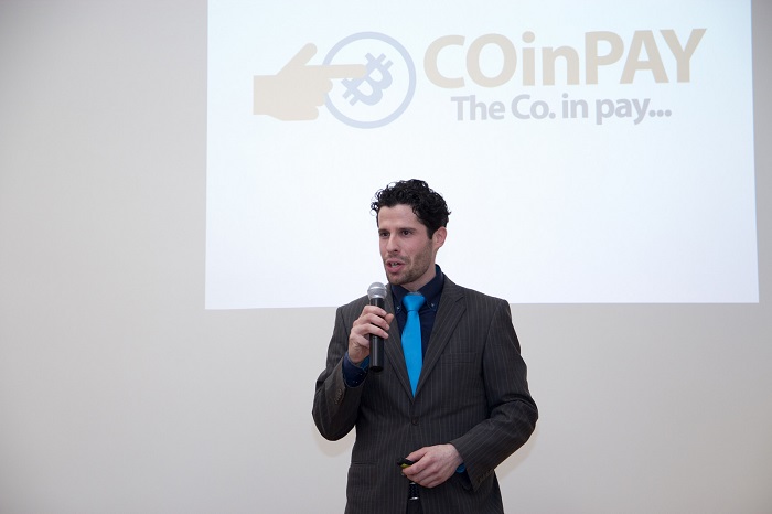 a man in a suit and blue tie is giving a speech about a cryptocurrency project