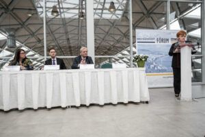 a woman is taking the stand and giving a speech while 3 other people are sitting and listening to her