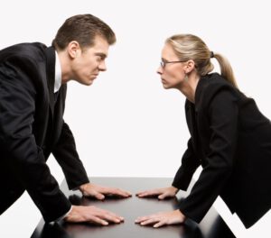 Caucasian mid-adult businessman and woman staring at each other with hostile expressions.